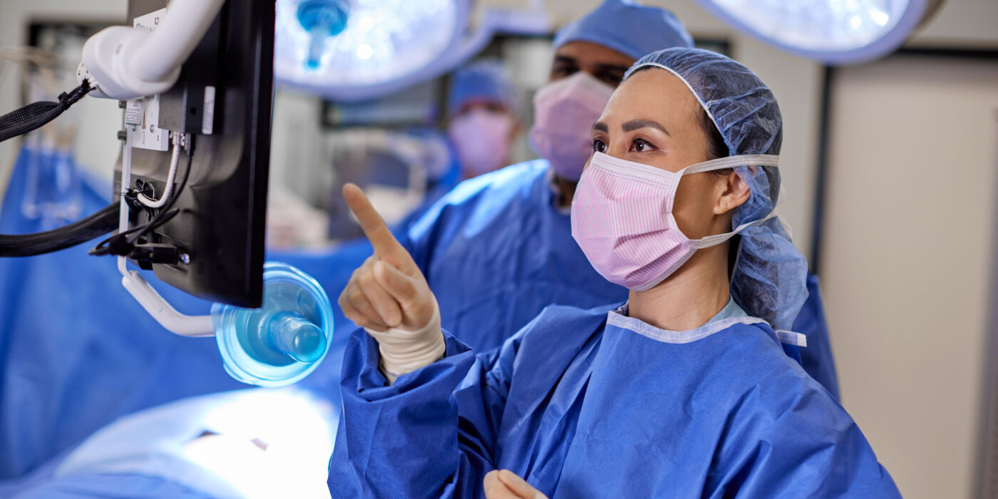 Nurses in scrubs and mask in surgical room reviewing information on computer monitor