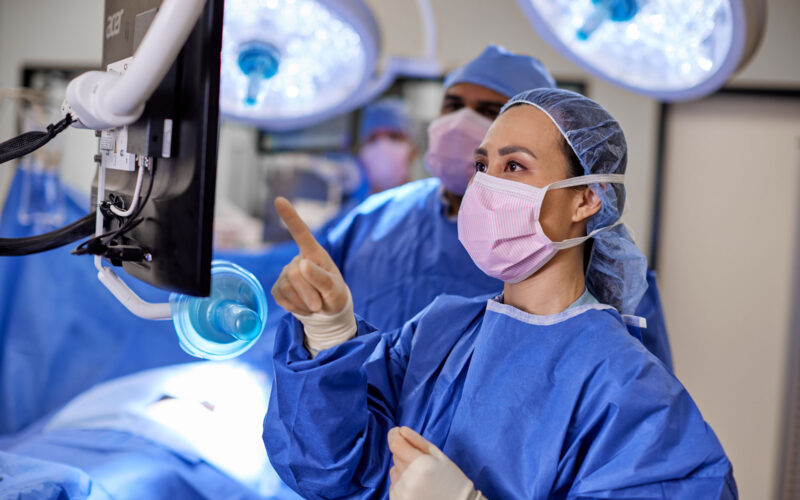 Nurses in scrubs and mask in surgical room reviewing information on computer monitor