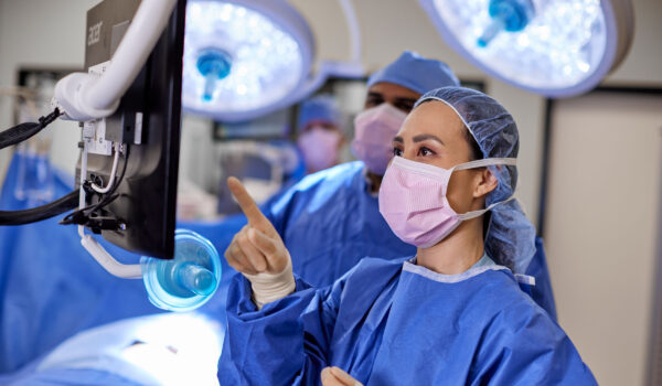 Nurses in scrubs and mask in surgical room reviewing information on computer monitor
