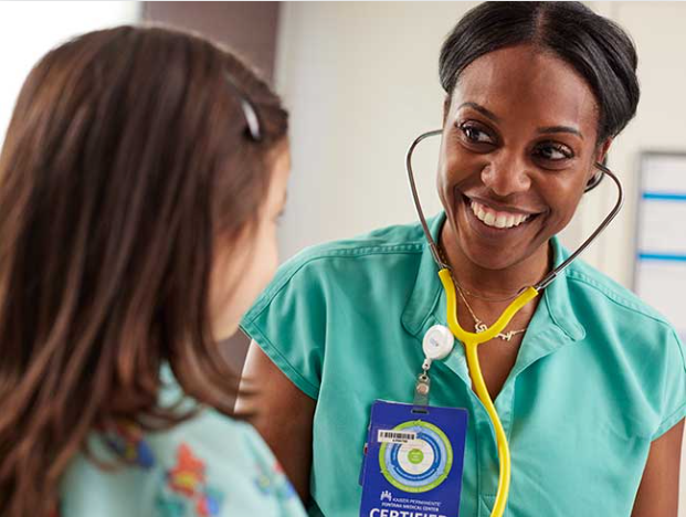 A nurse wearing a stethoscope smiling at her child patient.